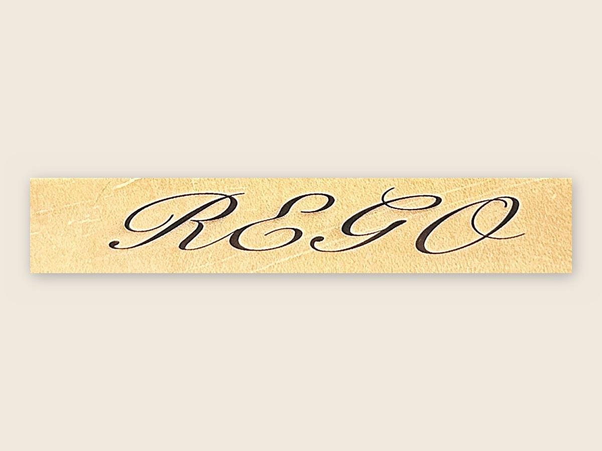 A strap of tan vegetable-tanned leather with REGO engraved into it in flowing script.